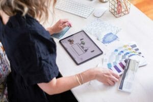 Emma Blomfield immerses herself in fabric swatches and uses a virtual decorating app on her tablet, accompanied by a keyboard and pen on the desk, bringing the intricate world of interior design to life.