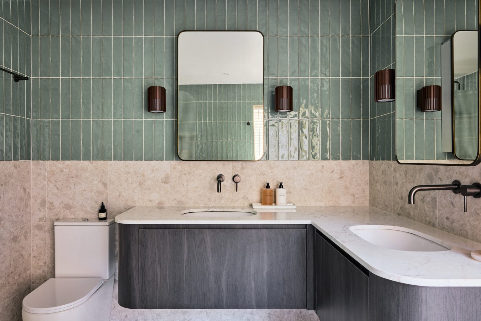 A modern Pymble bathroom with green vertical tiles, double marble sinks, twin mirrors, and sleek wall-mounted black fixtures.