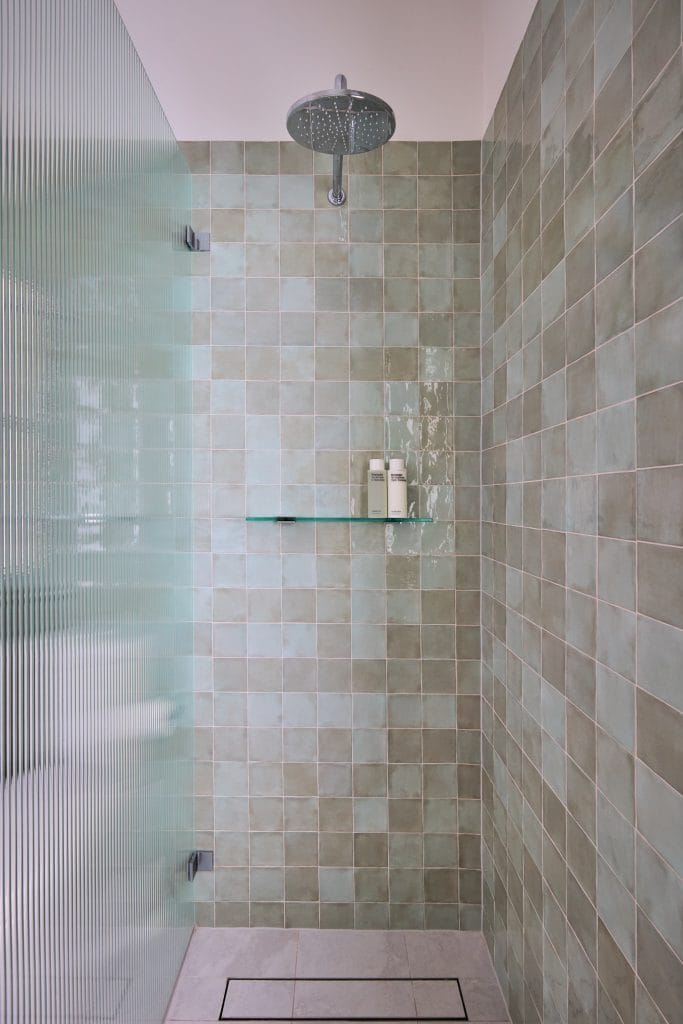 Sleek shower with greenish square tiles, rainfall showerhead, glass partition, wall shelf, and two bottles—ideal for a chic Mosman update.