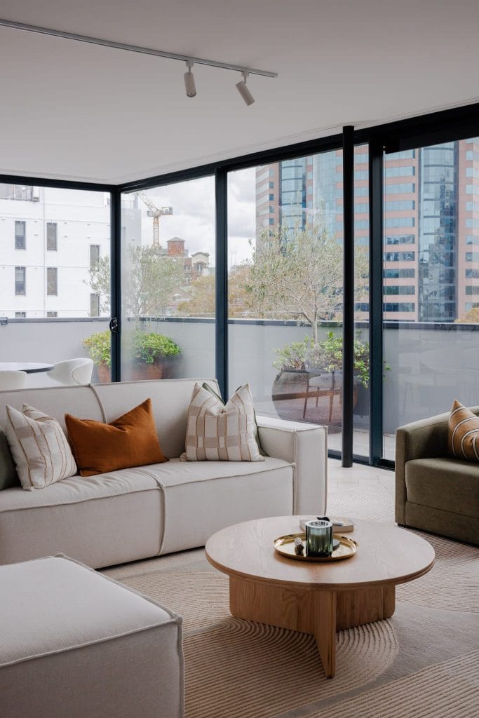 A stylish living room features neutral furniture, accent pillows, a wooden coffee table, and city views—ideal for bachelor pads.