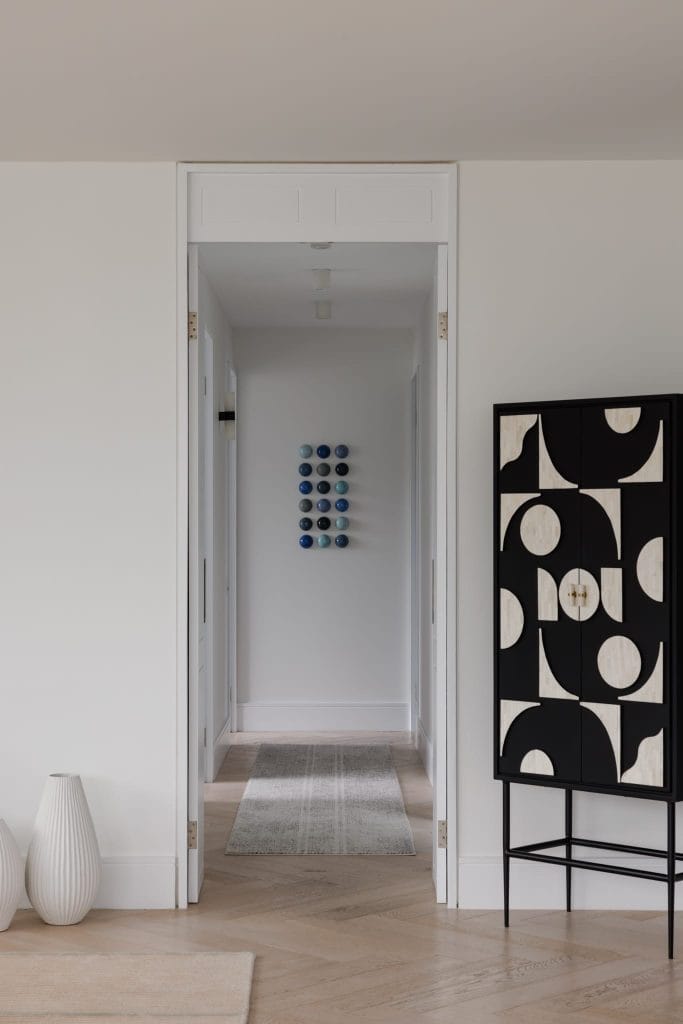 A sleek EB Studio hallway showcases light walls, a black and white geometric cabinet, two white vases, and circular wall art.