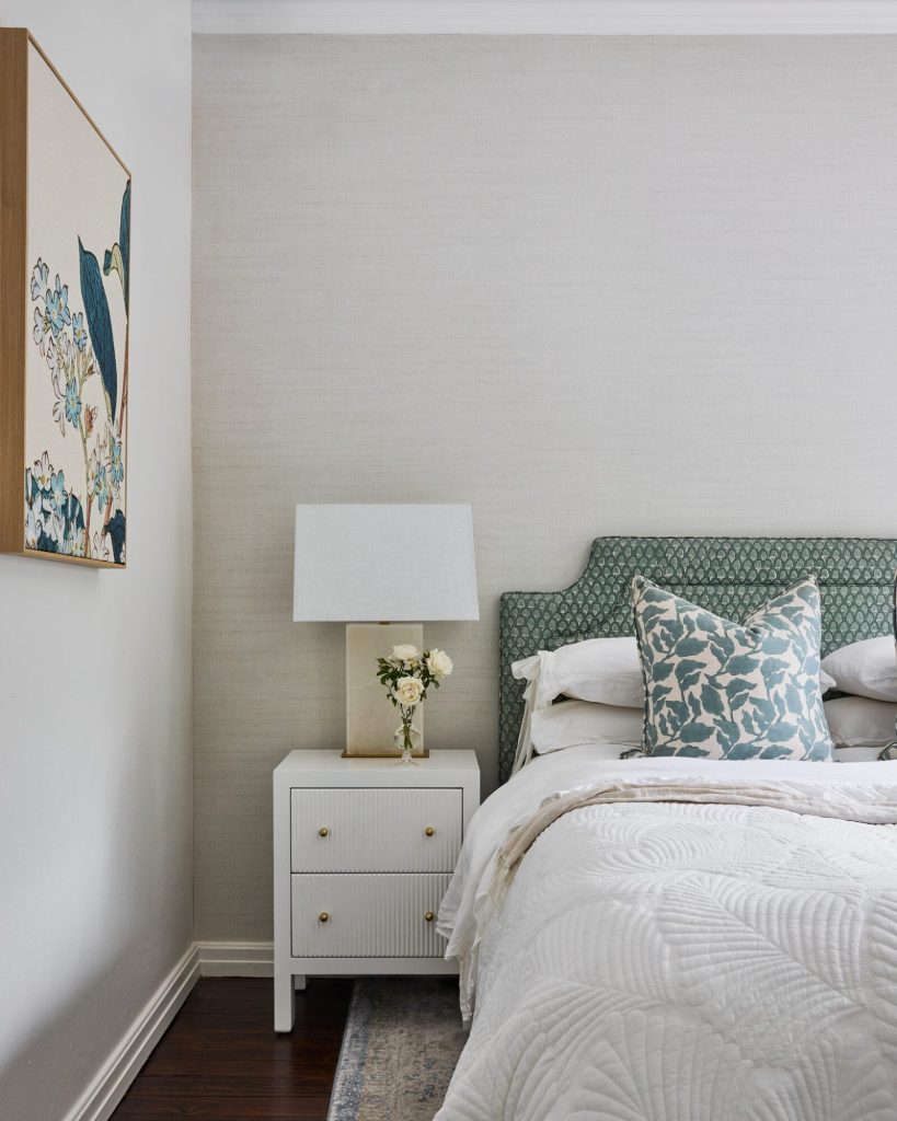 A modern bedroom styled by Interior Design Mosman features a green headboard, white nightstand, fresh flowers, and artful decor.