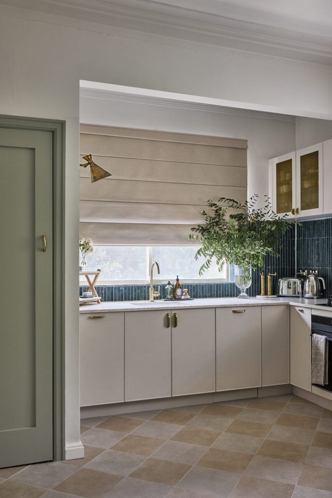 A Federation-style kitchen with white cabinets, green tiled backsplash, beige Roman shade, and a checkerboard floor.
