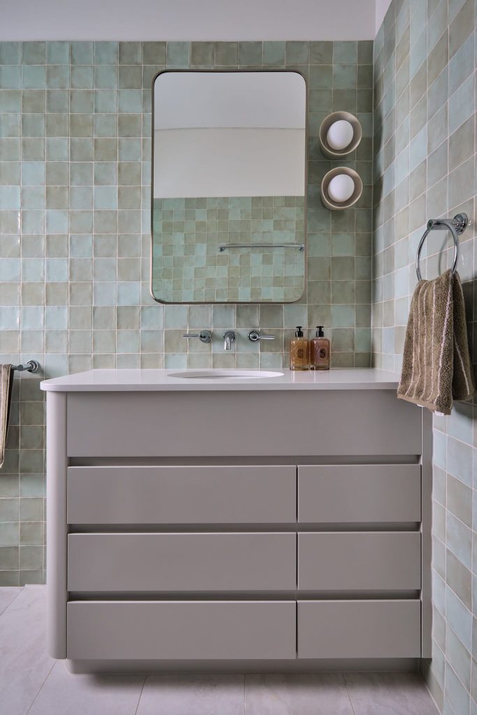 A sleek Federation Homes bathroom with a gray vanity, green tiles, brown towels, and round lights highlights Mosman style.