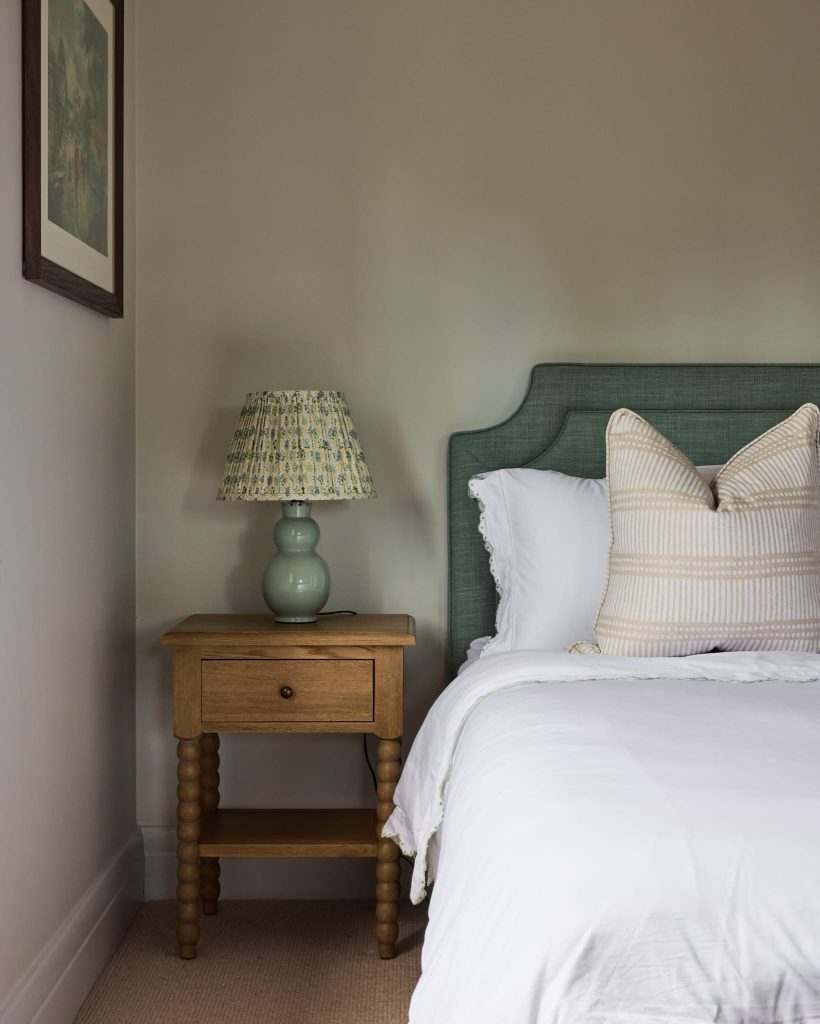 A cozy retreat features a neatly made bed with white linens, striped pillows, a wooden nightstand, and a green table lamp.