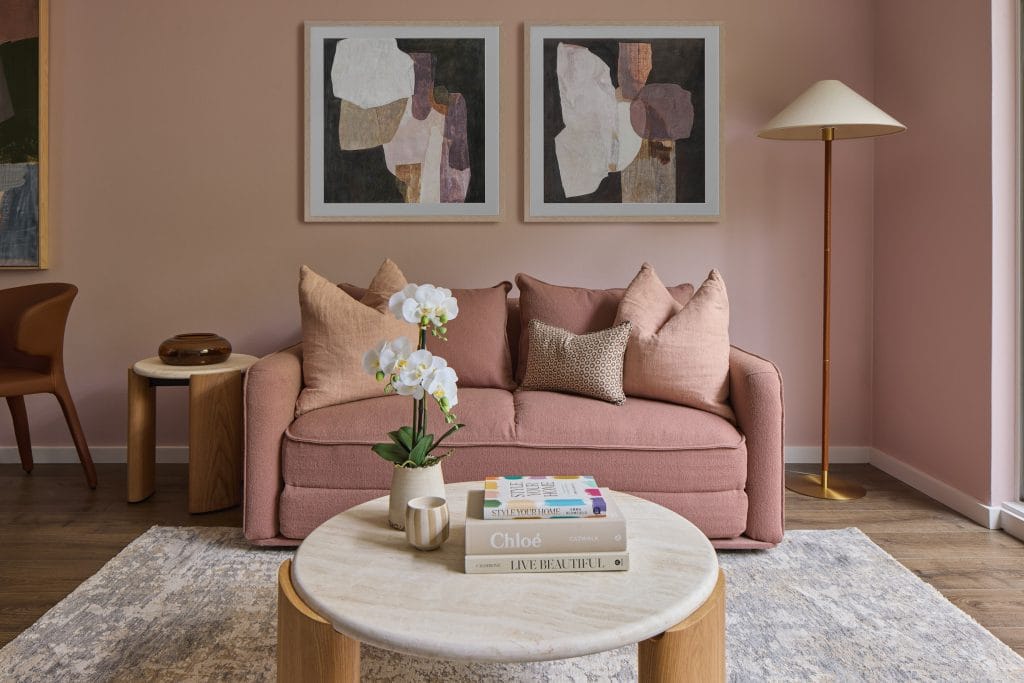 A pink sofa, abstract art on a pink wall, and a round coffee table with books and an orchid create a stylish bachelor pad vibe.