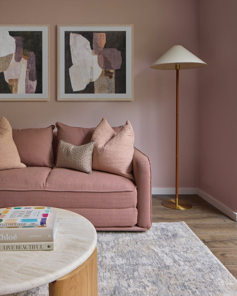 A stylish living room by EB Studio showcases a pink sofa, abstract art, gold floor lamp, round coffee table, and gray rug on wood floors.