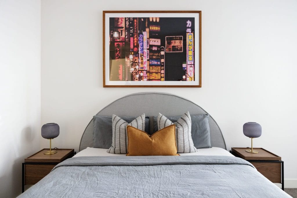 A tidy bed with gray and mustard pillows, matching lamps on bedside tables, and a city lights photo above the headboard.