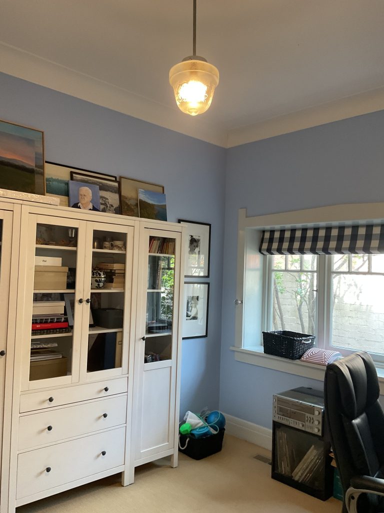 A Mosman home office with blue walls, white cabinets, framed photos, a striped shade, and office supplies—freshly updated.