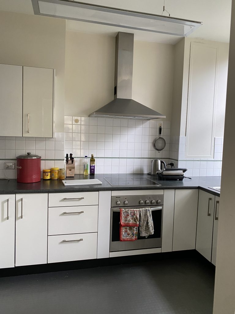 A modern kitchen features white cabinets, an electric stove and oven with two towels, and neatly organized countertop appliances.
