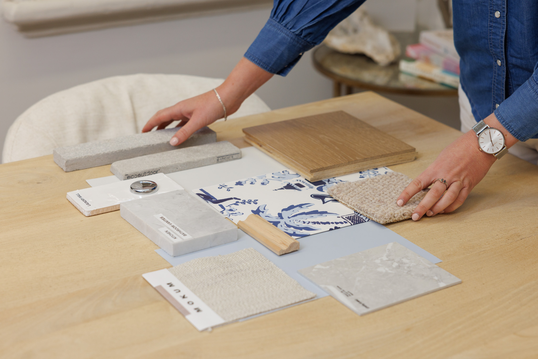 Emma Blomfield arranges material samples, including stone, wood, fabric swatches, and tile patterns, on a wooden table.
